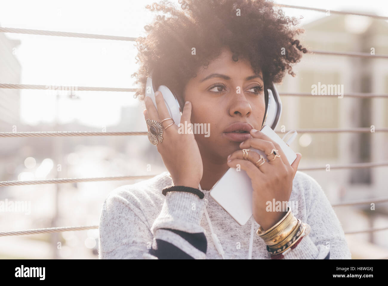 Young beautiful afro woman outdoor in city back light listneing music with head phone and smart phone hand hold, thoughtful - me Stock Photo