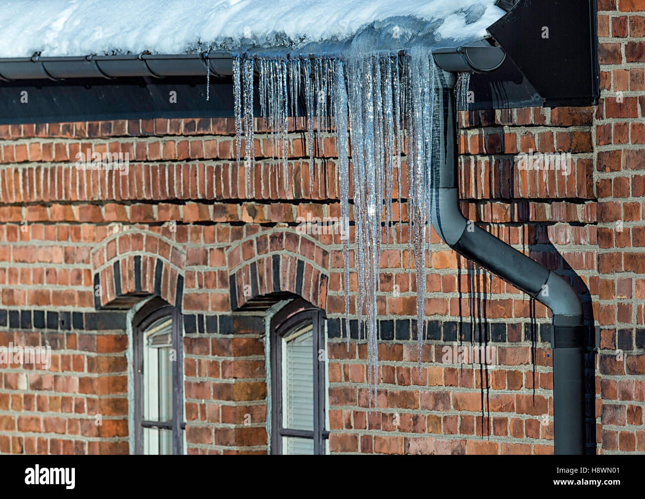 ice needles with Water Spout with brick walled building. Stock Photo