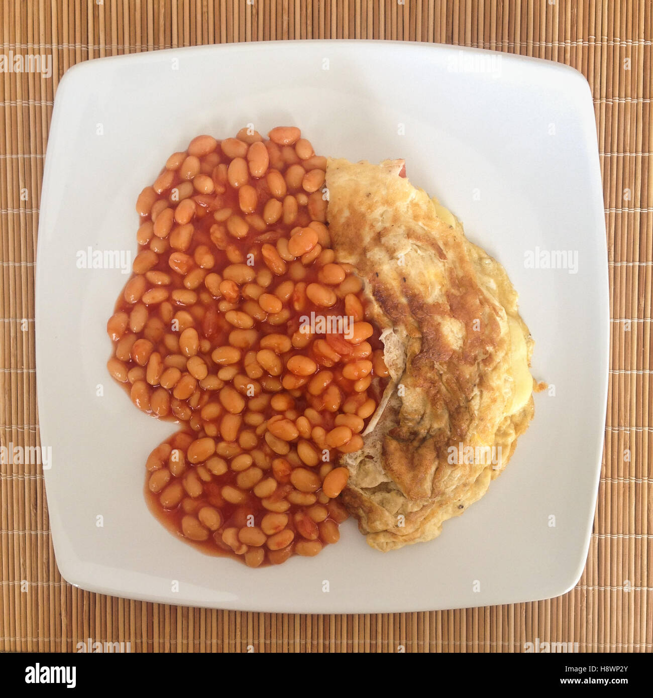 baked beans and omelette on a square white plate from above on a wicker place mat. Mobilestock Stock Photo