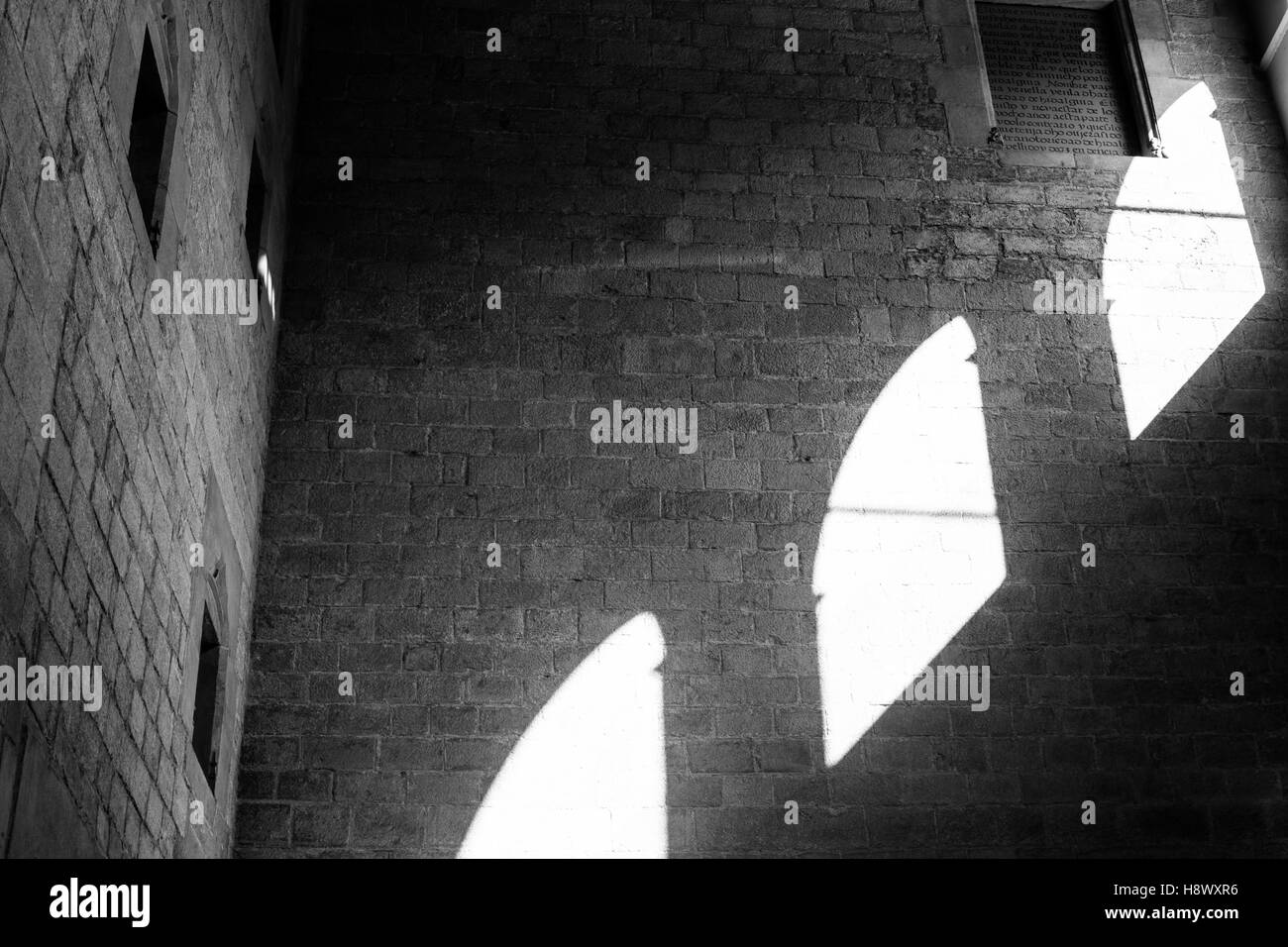 Black and white stone wall with sunlight coming through three windows. Stock Photo