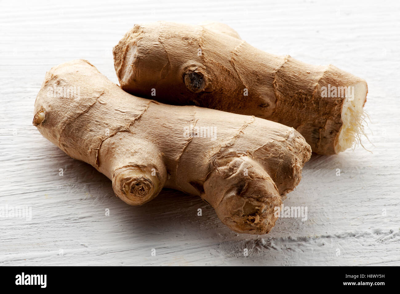 Fresh raw root ginger on a textured white board for use in cooking as a healthy pungent aromatic seasoning Stock Photo