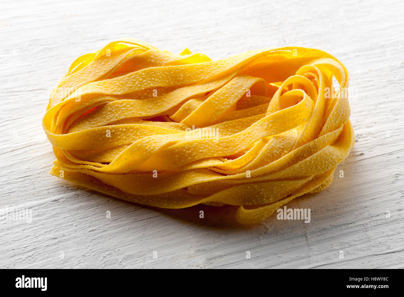 Roll of raw Italian tagliatelle pasta or ribbon noodles for traditional mediterranean cuisine in a close up view on a white wood Stock Photo
