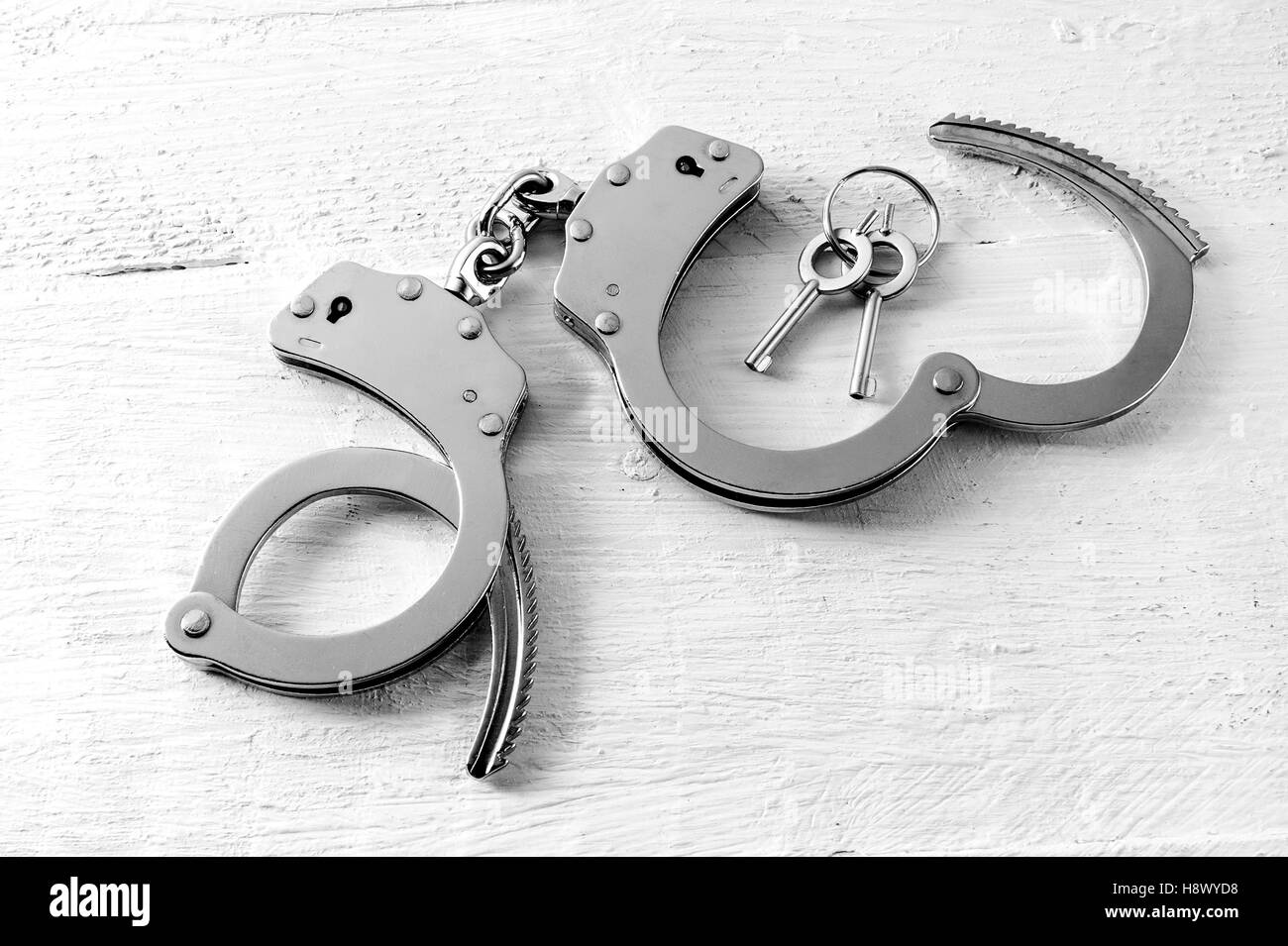 Pair of open handcuffs with the keys alongside lying on a textured white wooden board in a close up high angle view Stock Photo