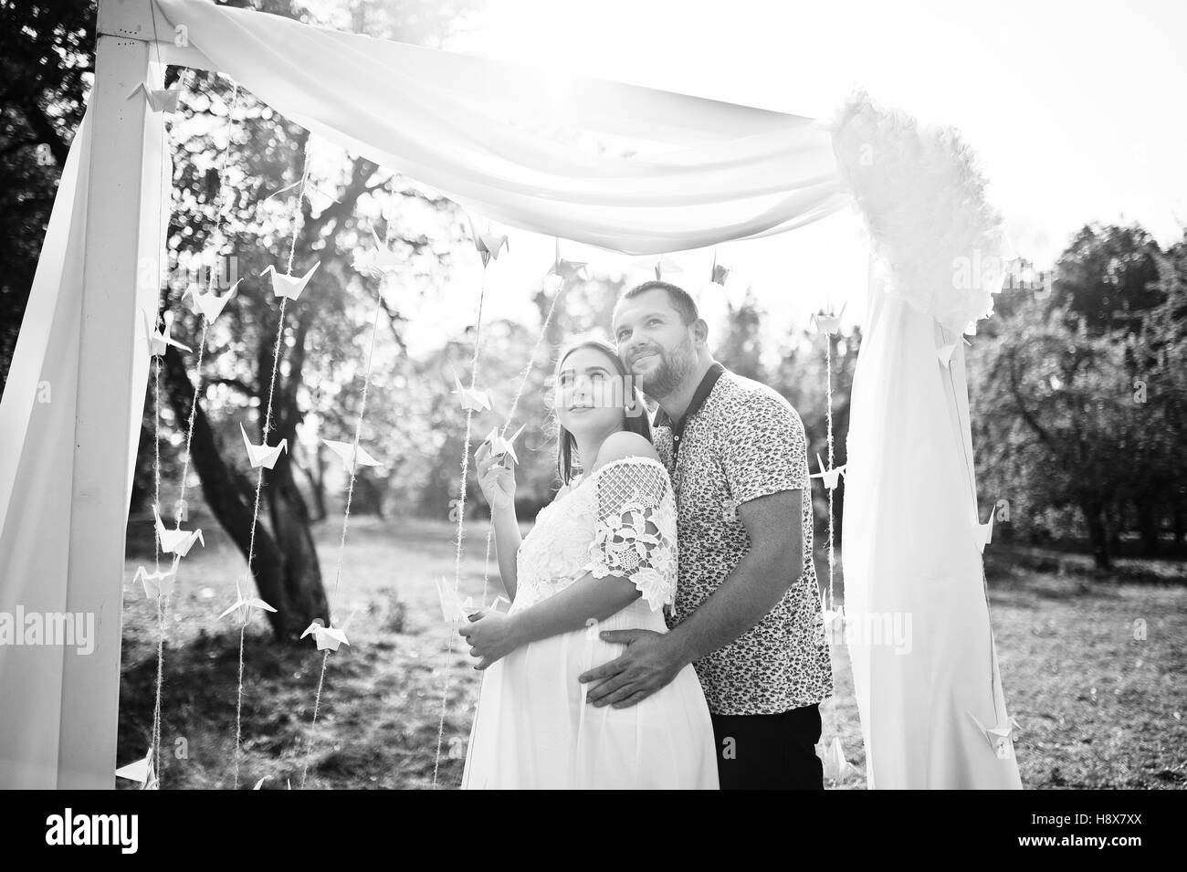 Happy pregnant couple stay hugging and loving near decor arch at garden on sunny day. Stock Photo