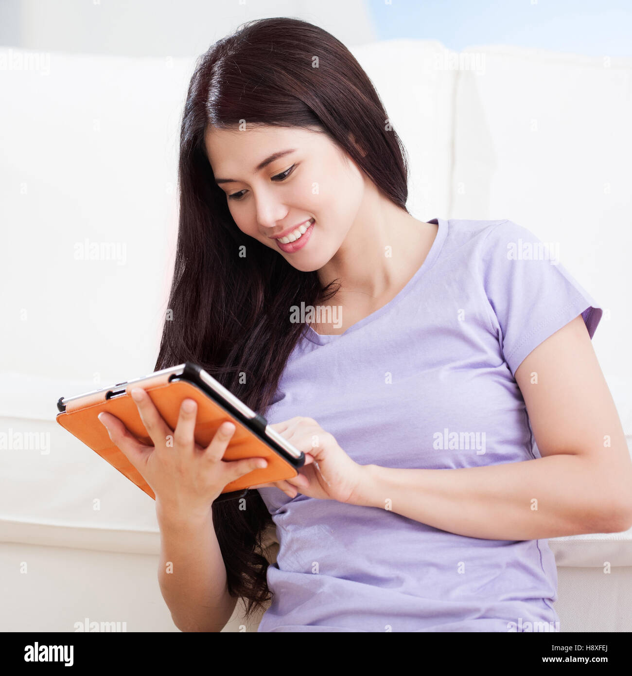 Young smiling Asian woman sitting on floor and working with tablet pc ...