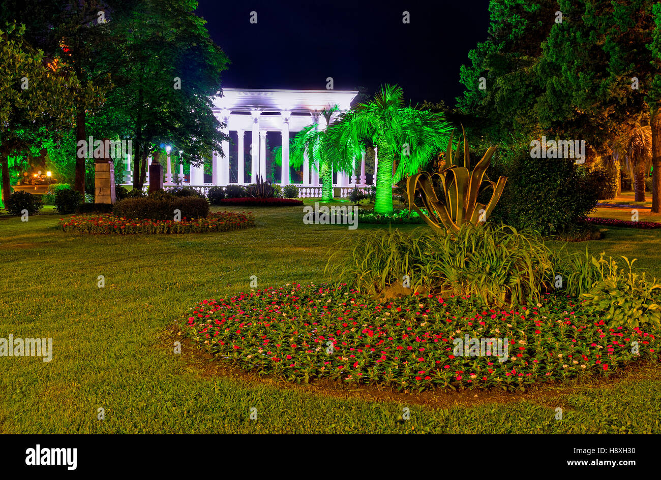 The colorful flower beds, illuminated palms and dark trees in the evening Seaside Park of Batumi, Georgia. Stock Photo