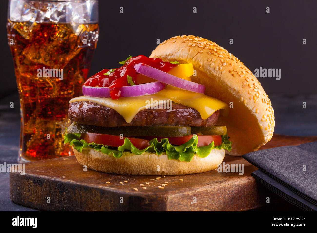 A delicious homemade cheeseburger with red onions, pickles, tomato, lettuce and ketchup. Stock Photo