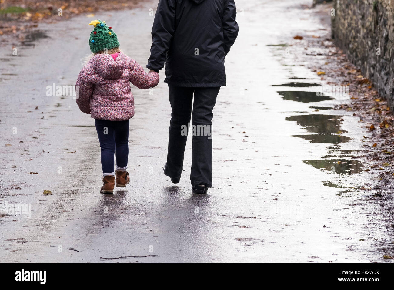 A child and an adult walking hand in hand down a road. Stock Photo