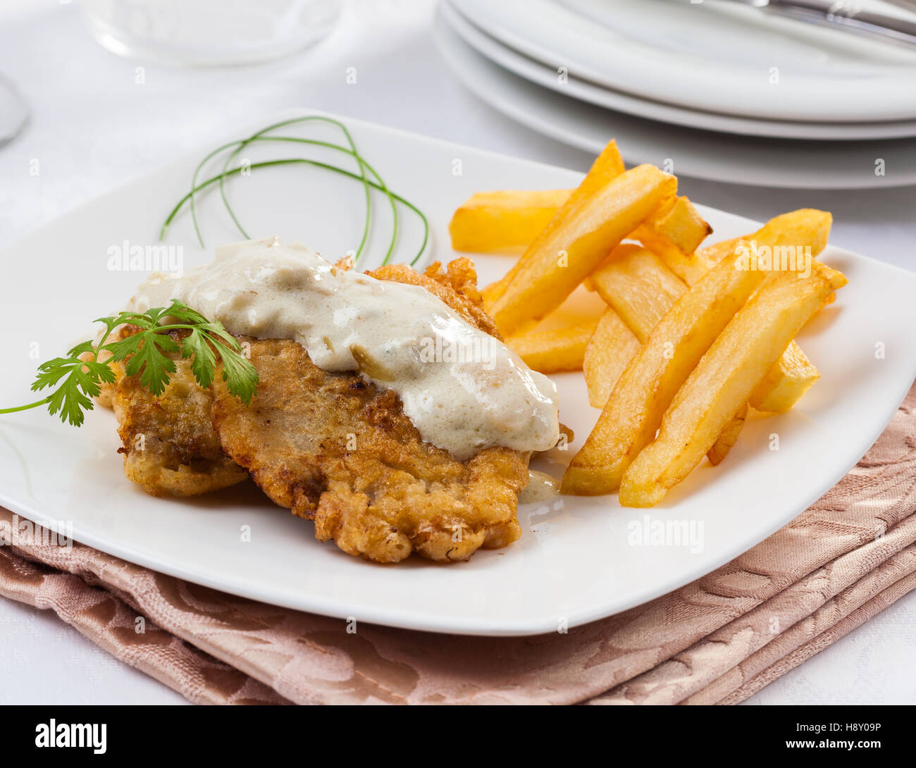 Breaded cutlet with blue cheese sauce and fried potatoes. Stock Photo