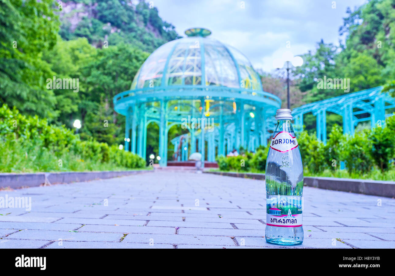 The glass bottle of Borjomi mineral water with the natural water source under pavilion on the background Stock Photo