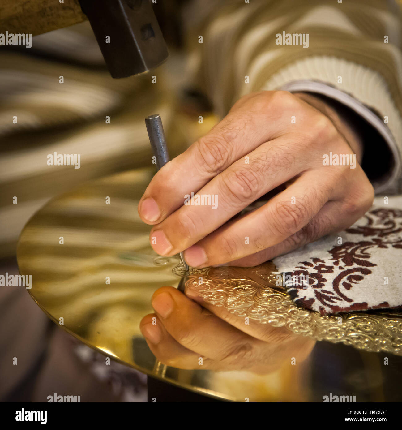 Abdelgabar Guernani raises his hammer to strike an ornament into a brass plate in his workshop in Fès, Morocco. Stock Photo