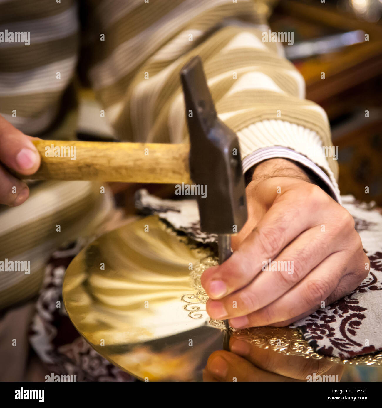 Brass craftsman Abdelgabar Guernani hammers an ornament into a brass plate with a chisel in his workshop in Fès, Morocco. Stock Photo