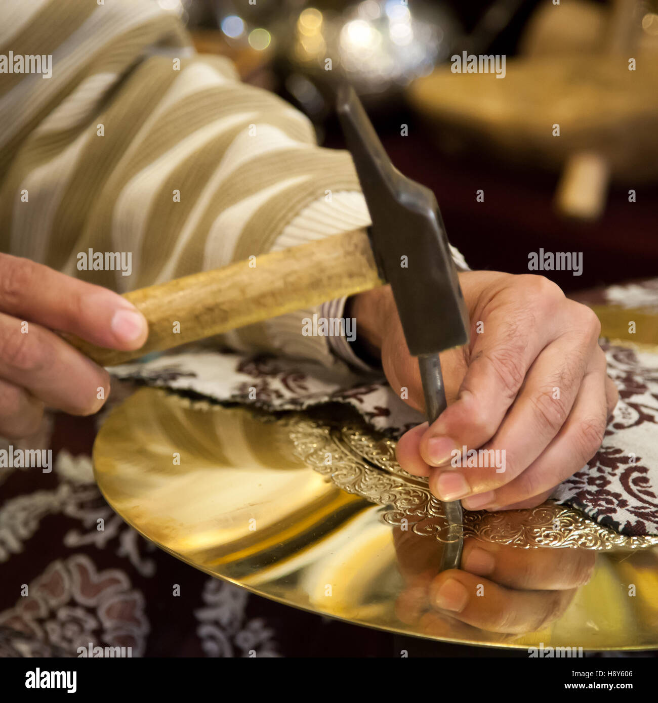 Abdelgabar Guernani engraves an ornament into a brass plate with hammer and chisel. The brass craftsman works in his workshop in Fès, Morocco. Stock Photo