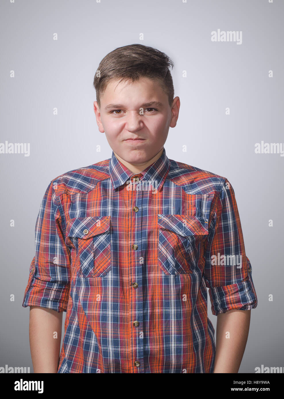 Angry, aggressive teenager on gray-white background wearing a plaid shirt Stock Photo