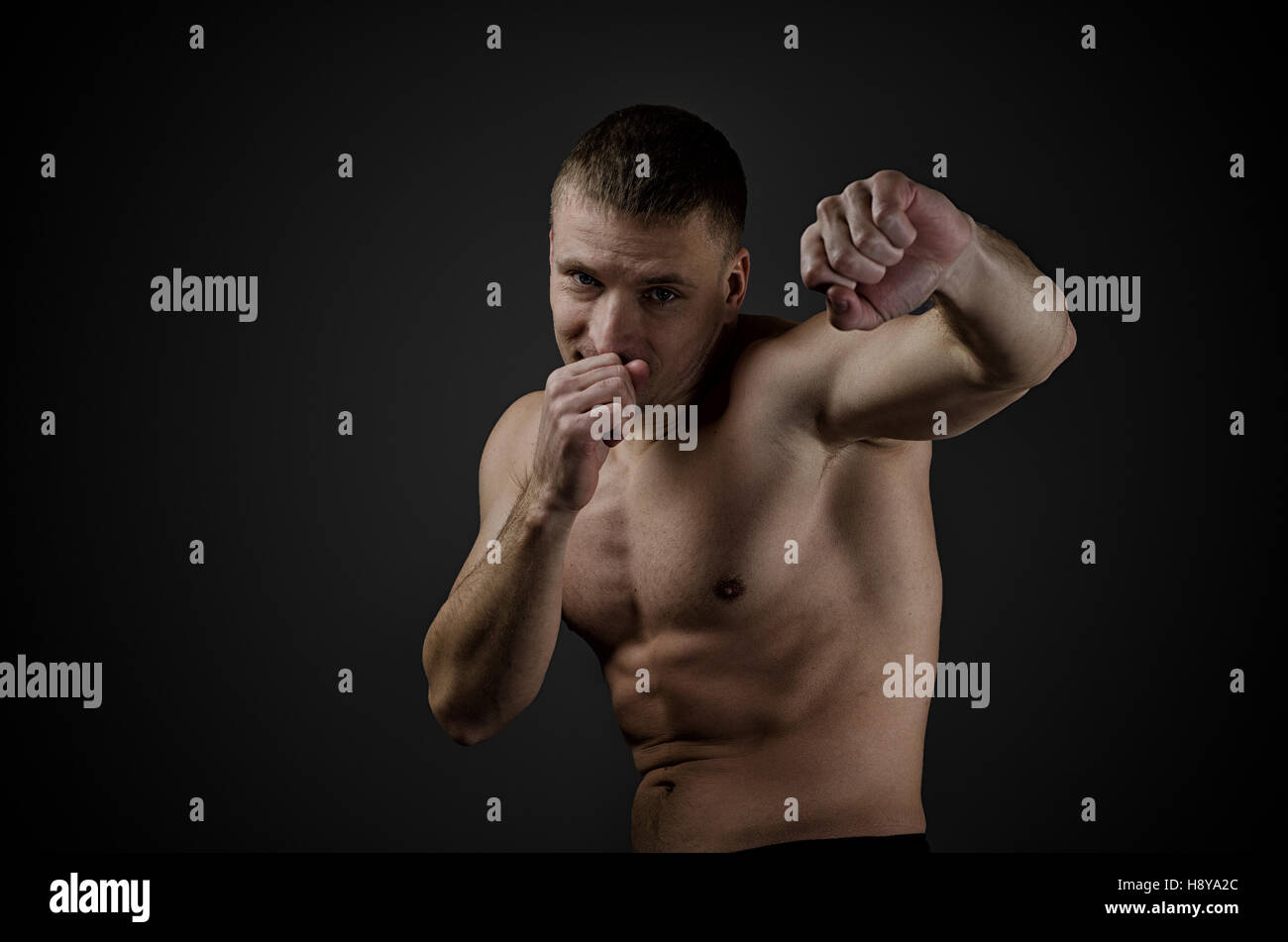Training Young muscular boxer on a black background. Practiced punches