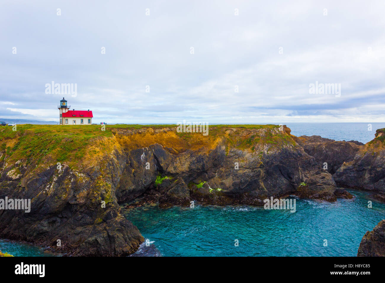 Distant view of rocky cliffs above ocean cove and the historic Point Cabrillo Light Station lighthouse on a cloudy evening in Me Stock Photo