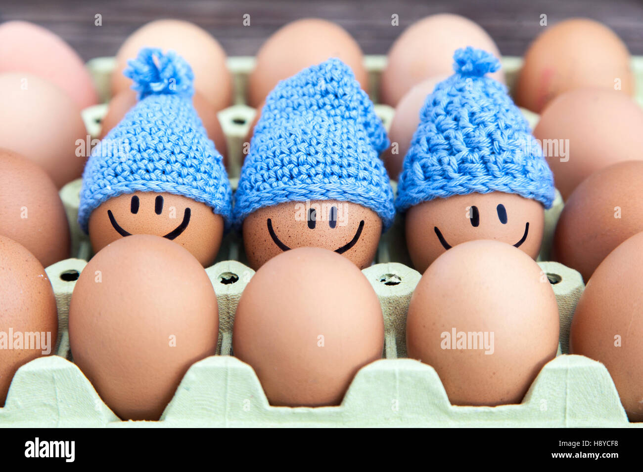 Three eggs wearing blue hats, stay together with happy faces. Stock Photo