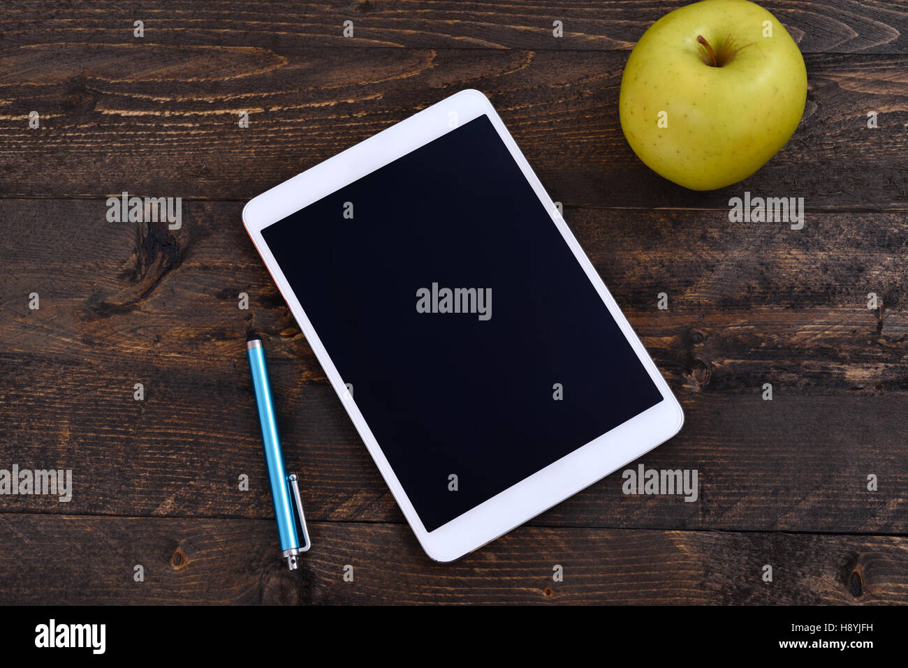 White digital tablet with black screen on wooden table, with a tablet pen and an apple Stock Photo