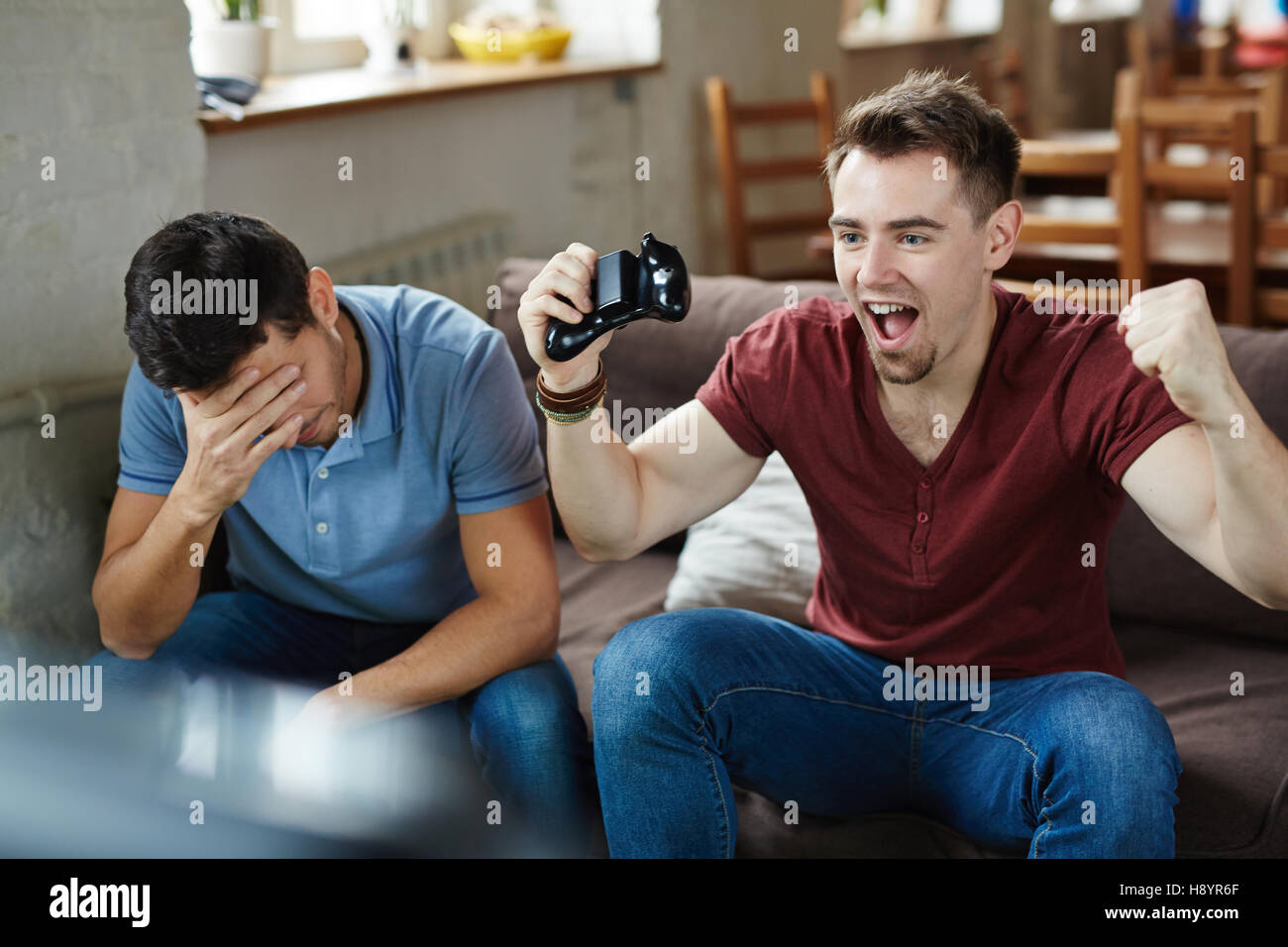 Ecstatic gameplayer expressing triumph with his defeated friend near by ...