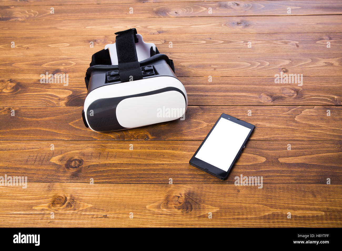 front side of a vr headset and a smart phone, isolated on wooden floor background, close up Stock Photo