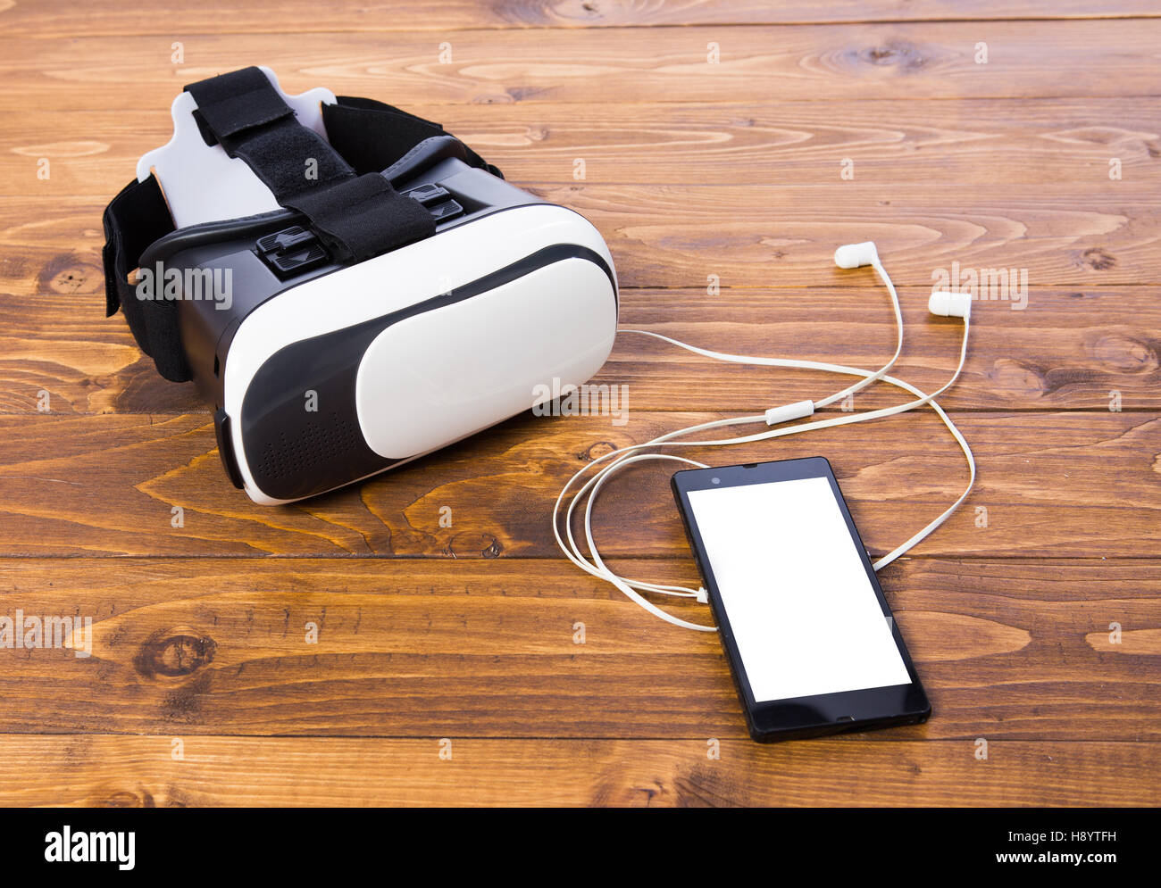 front side of a vr headset with earbuds and a smart phone, isolated on wooden floor background, close up Stock Photo