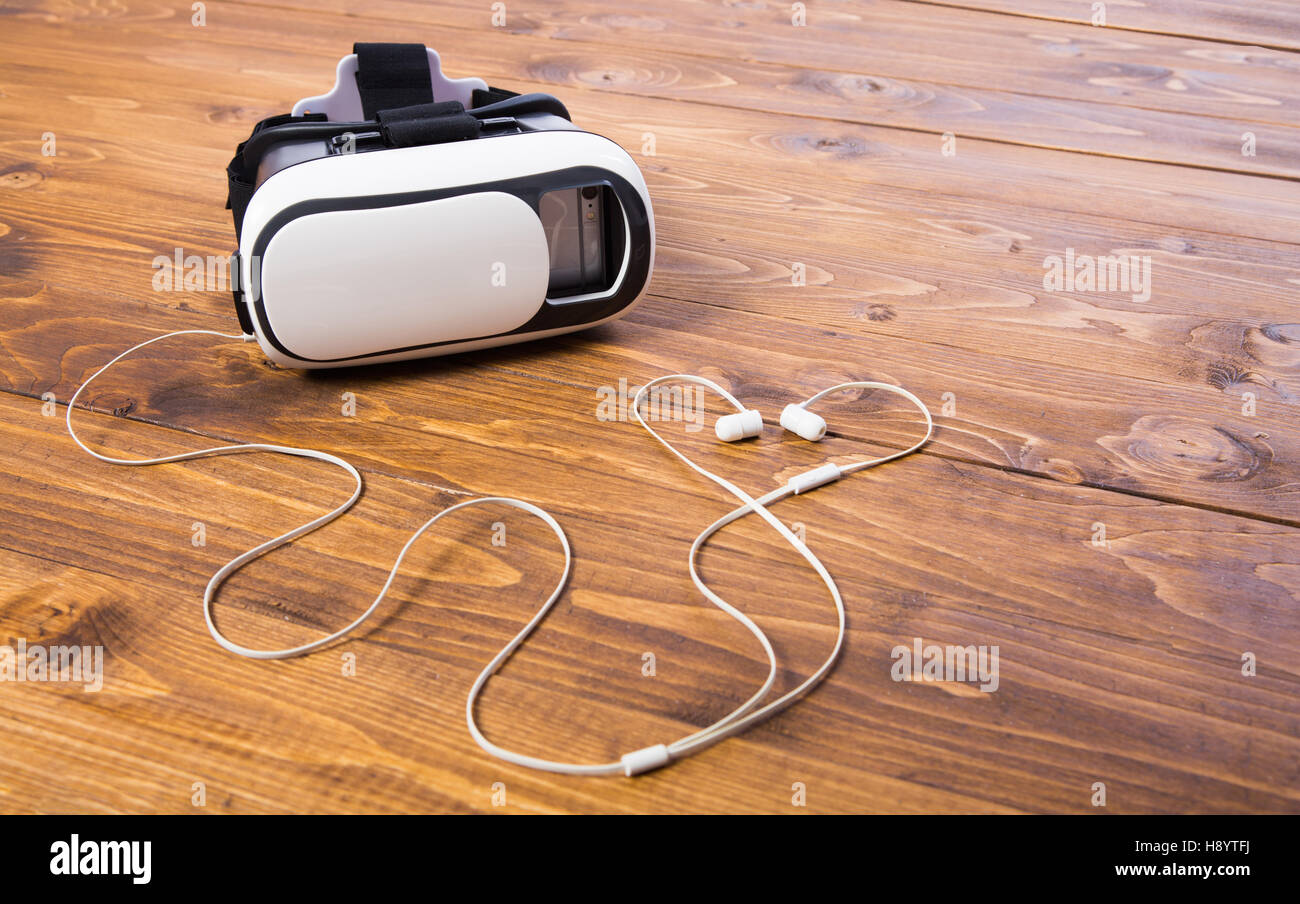 front side of a vr headset with earbuds , isolated on wooden floor background Stock Photo