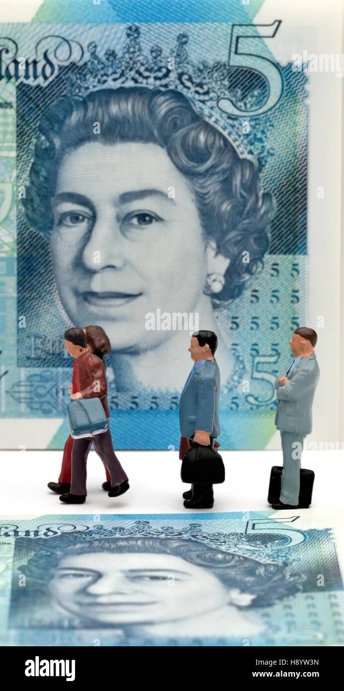 Miniature figurines walking in front of a five pound note. Stock Photo