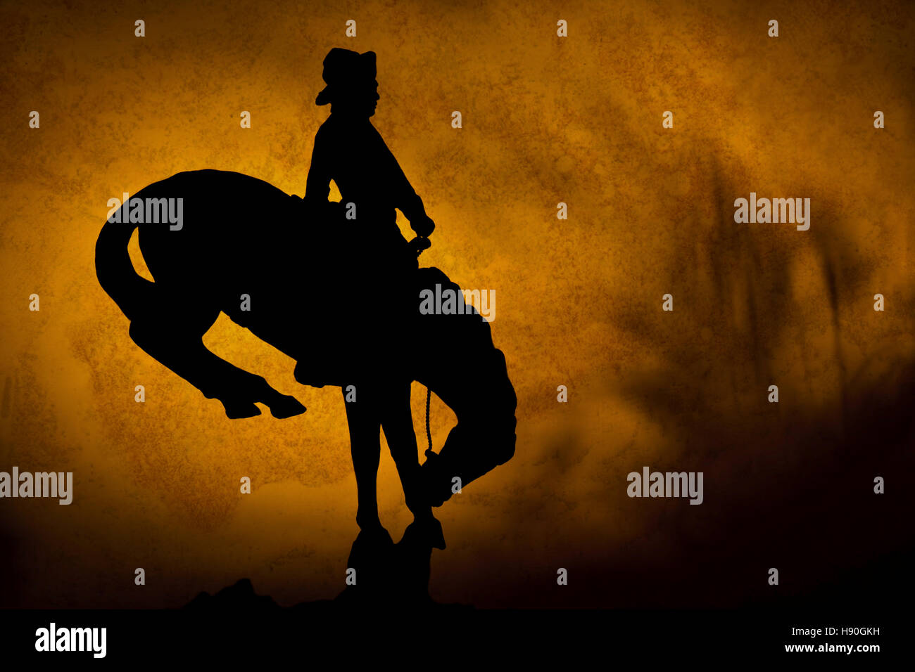 Silhouette of cowboy on a bucking bronco. orange yellow sunset background with shadows of prairie grass. Stock Photo