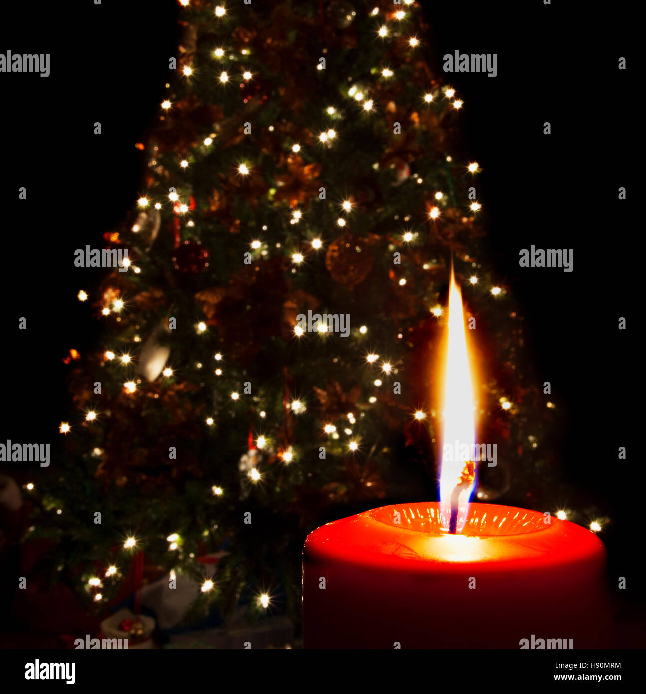 Single red candle burning in front of a lighted Christmas tree Stock