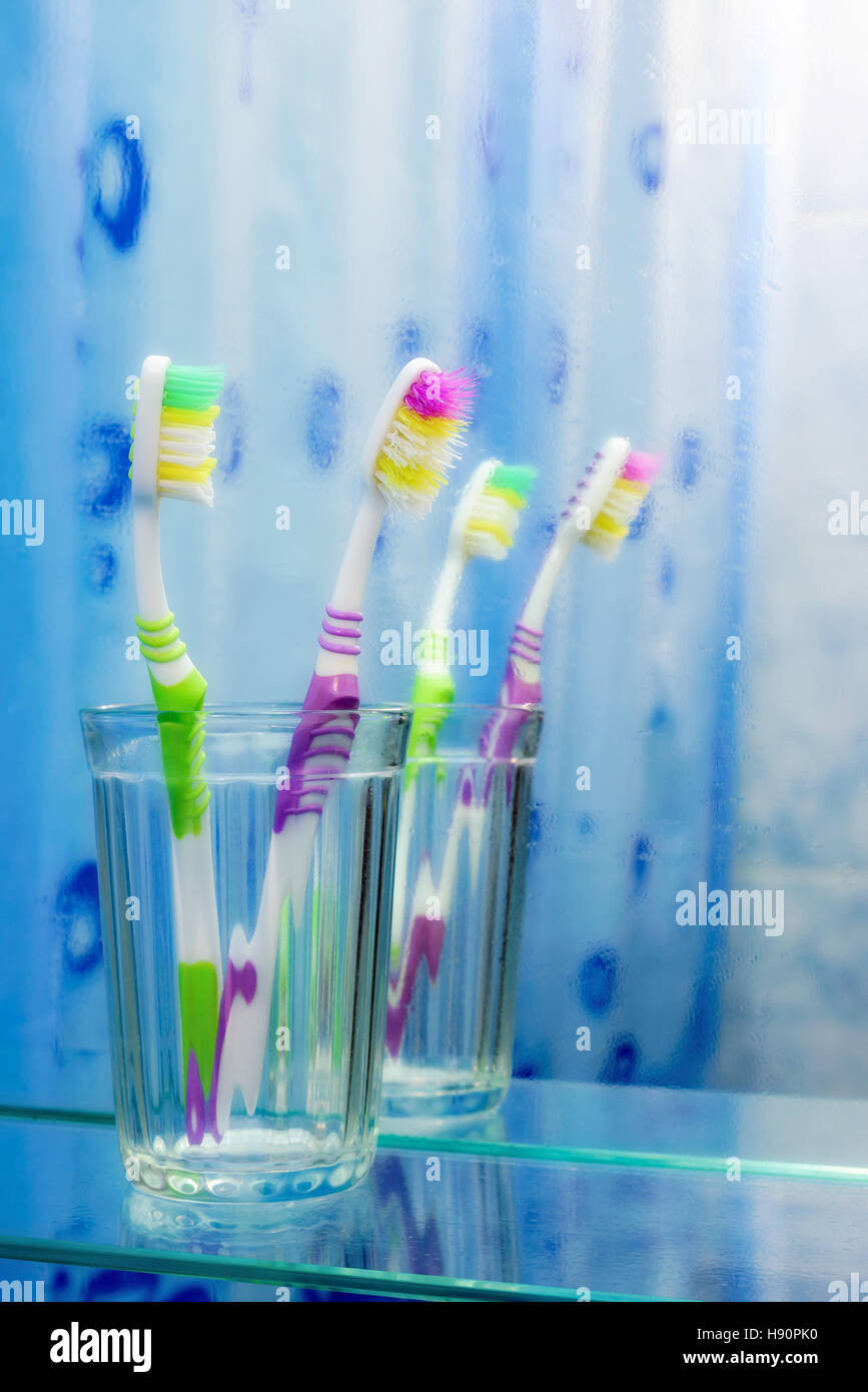 Two colorful toothbrushes in a glass, in front of the bathroom mirror covered with mist Stock Photo