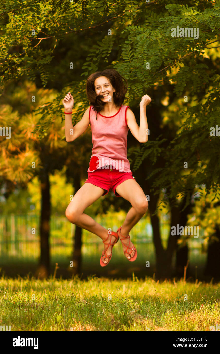 I did it ! Teenage girl in red jumps happily in the park in summer. Stock Photo