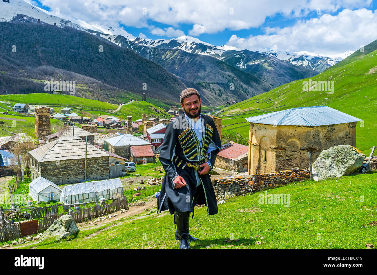 The young Svan in traditional costume poses with the village on the background Stock Photo