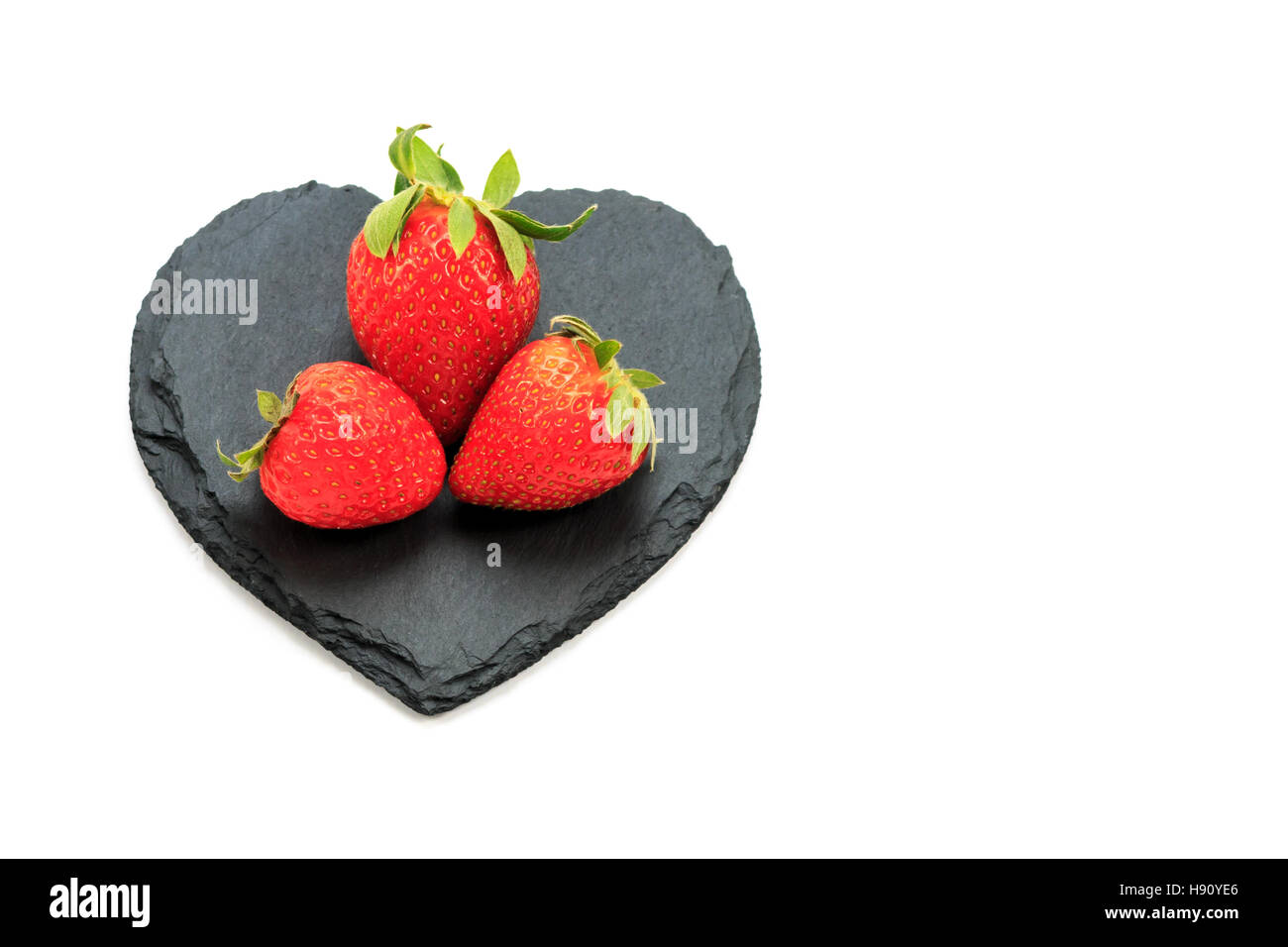 Trio of Strawberries on black heart-shaped slate Stock Photo