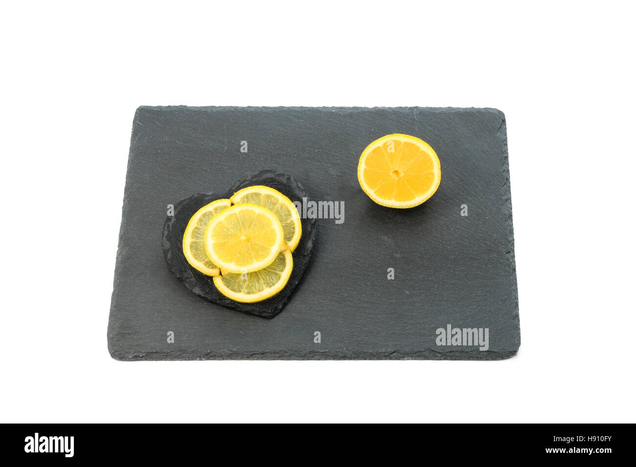 Lemon slices and half lemon on black slate board isolated on white background Stock Photo