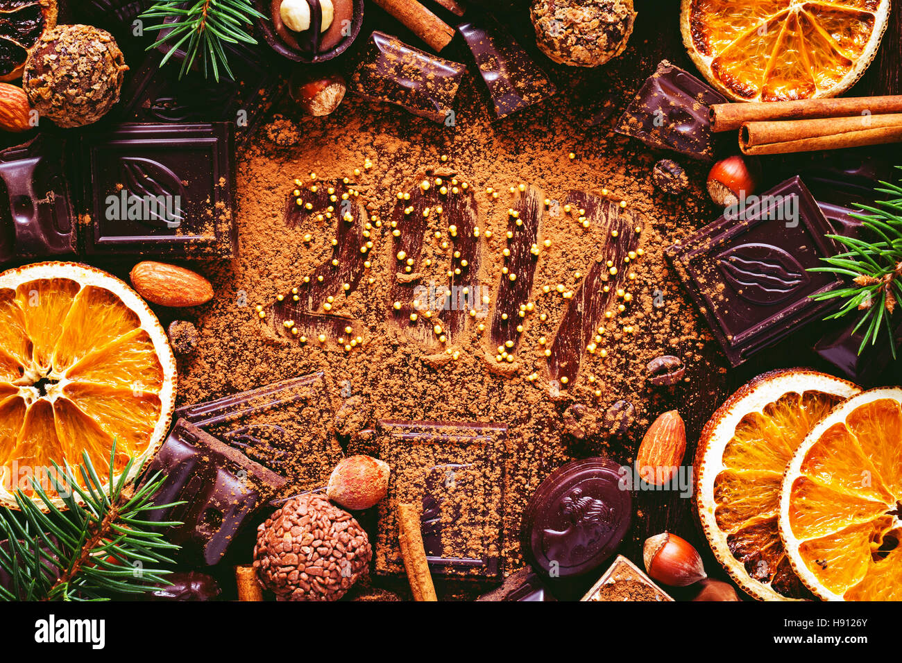 Greeting card for 2017 New Year! Chocolates, sweets, dried orange rings, nuts, spices and fir tree branches. Top view Stock Photo