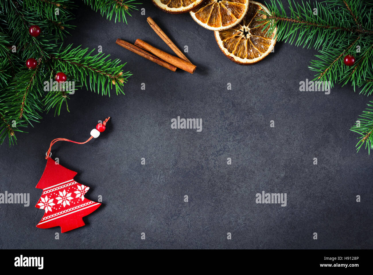 Background for Christmas or New Year: fir tree, cranberries, cinnamon and dry oranges over dark background. Copy space for text. Stock Photo