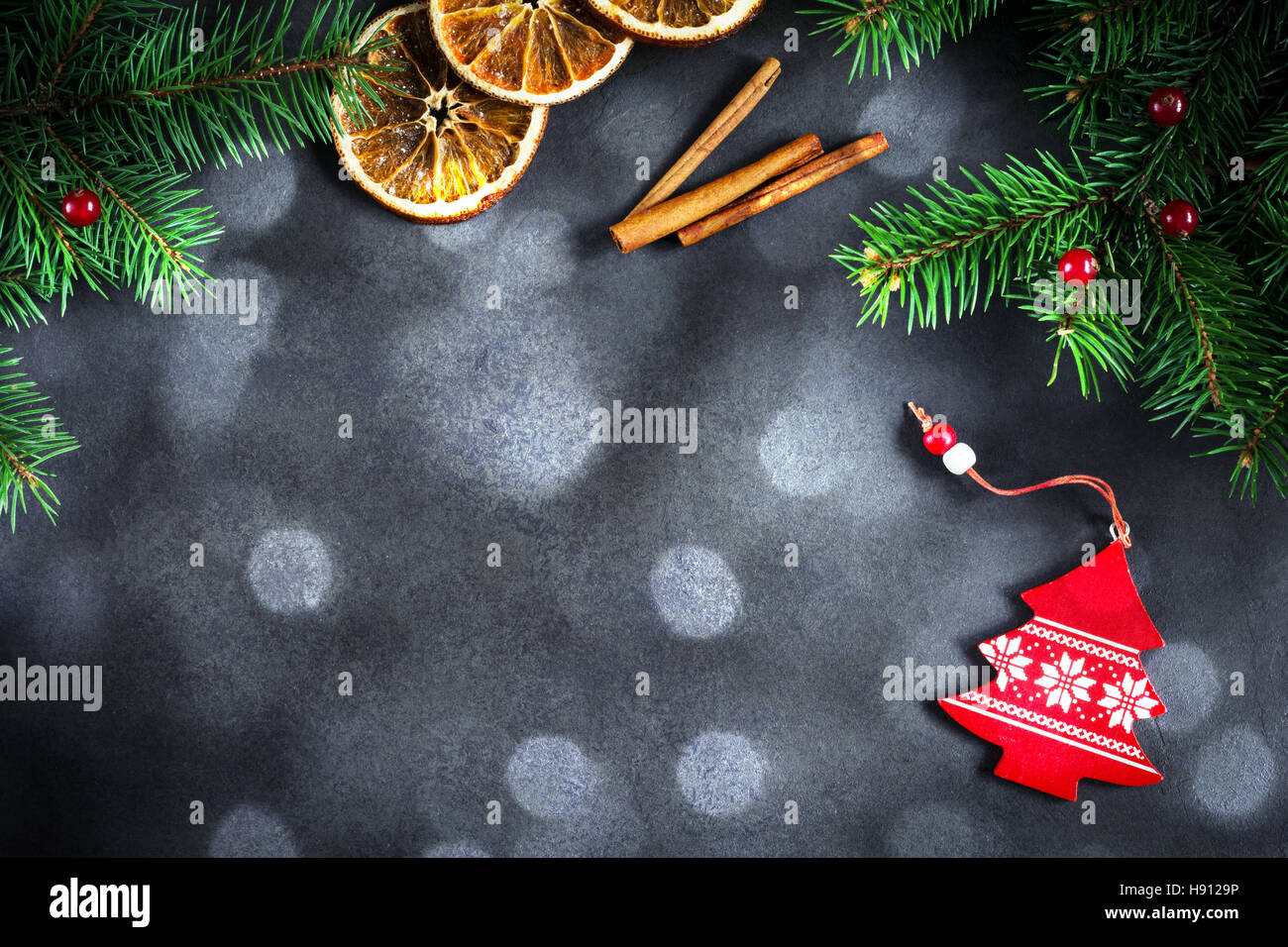 Background for Christmas or New Year: fir tree, cranberries, cinnamon and dry oranges over dark background. Copy space for text. Stock Photo