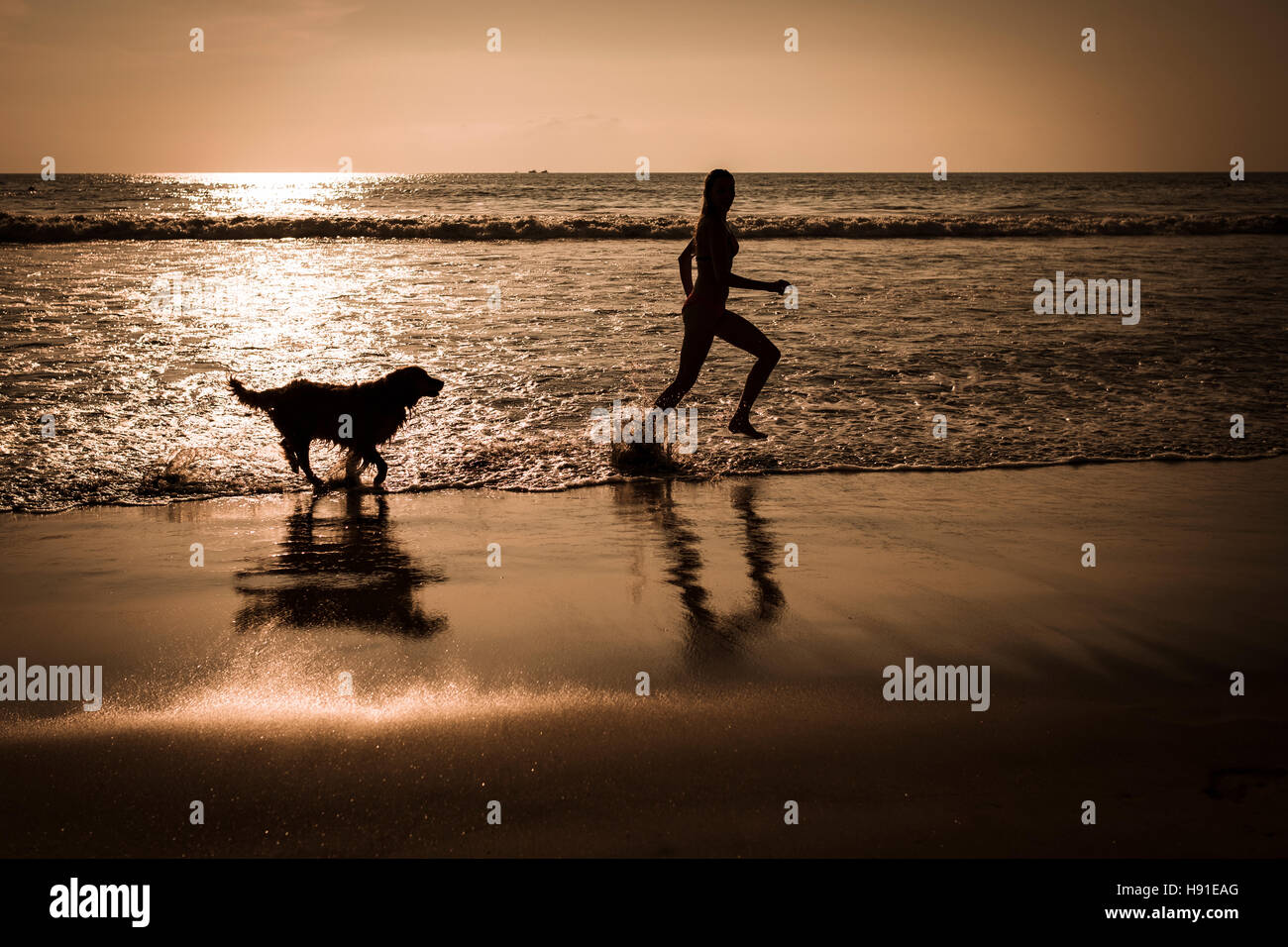 Silhouette of young woman running with dog at beach right before sunset. Riviera Nayarit, Mexico. Stock Photo