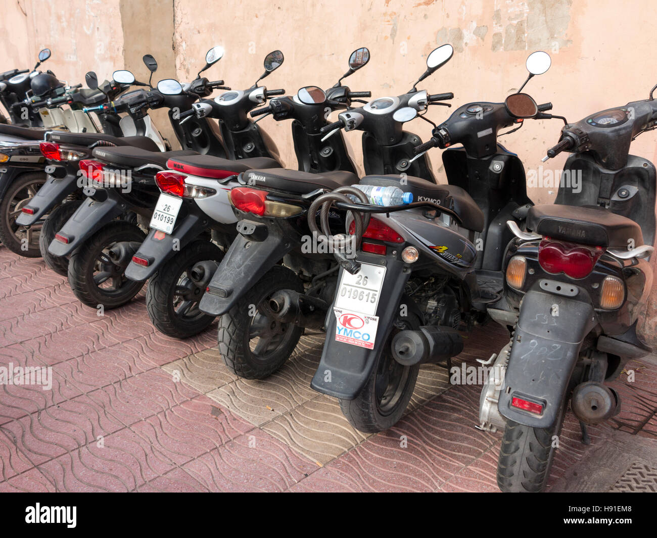 A row of neatly parked motor scooters on a Moroccan street pavement against a plain wall Stock Photo