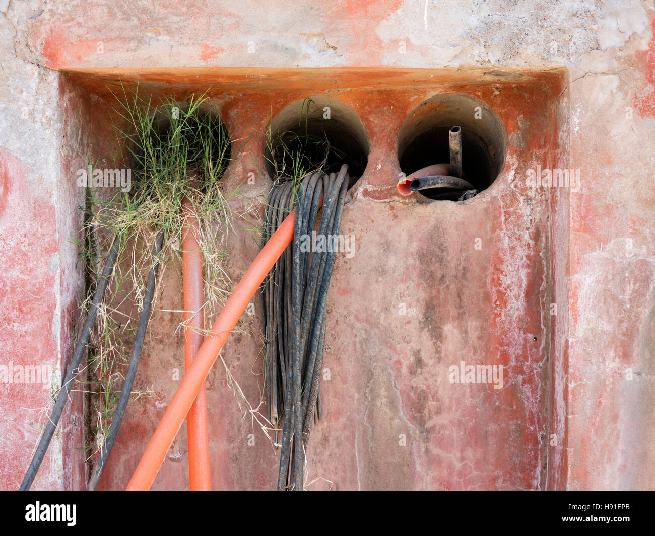 Tadelakt pink wall containing plastic piping emerging out of three circular outlets, with weed and water stains Stock Photo