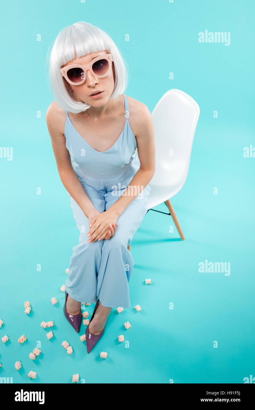 Top view of cute young woman in blonde wig and sunglasses sitting on the chair Stock Photo