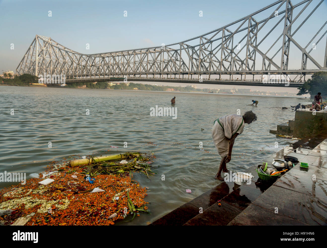 Old lady washes her utensils at Hooghly river bank near Howrah bridge. Stock Photo