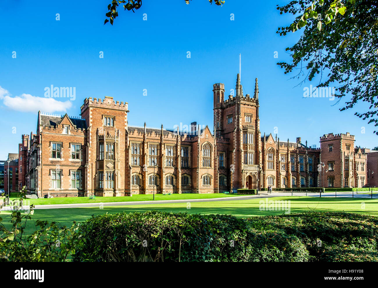The Queen's University of Belfast with a grass lawn, tree branches and a hedge in sunset light Stock Photo