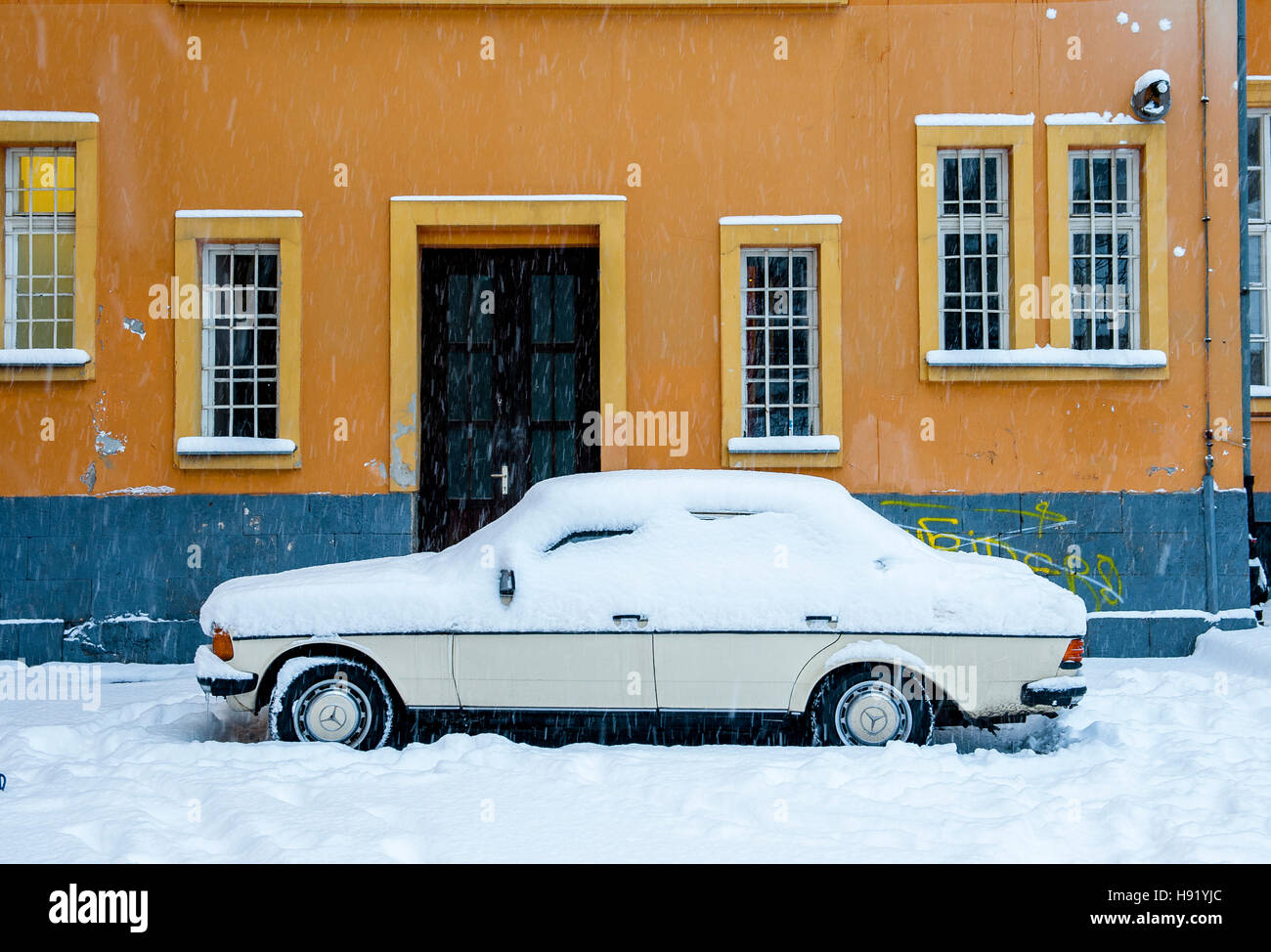 Old car covered with snow parked in front of orange wall building Stock ...