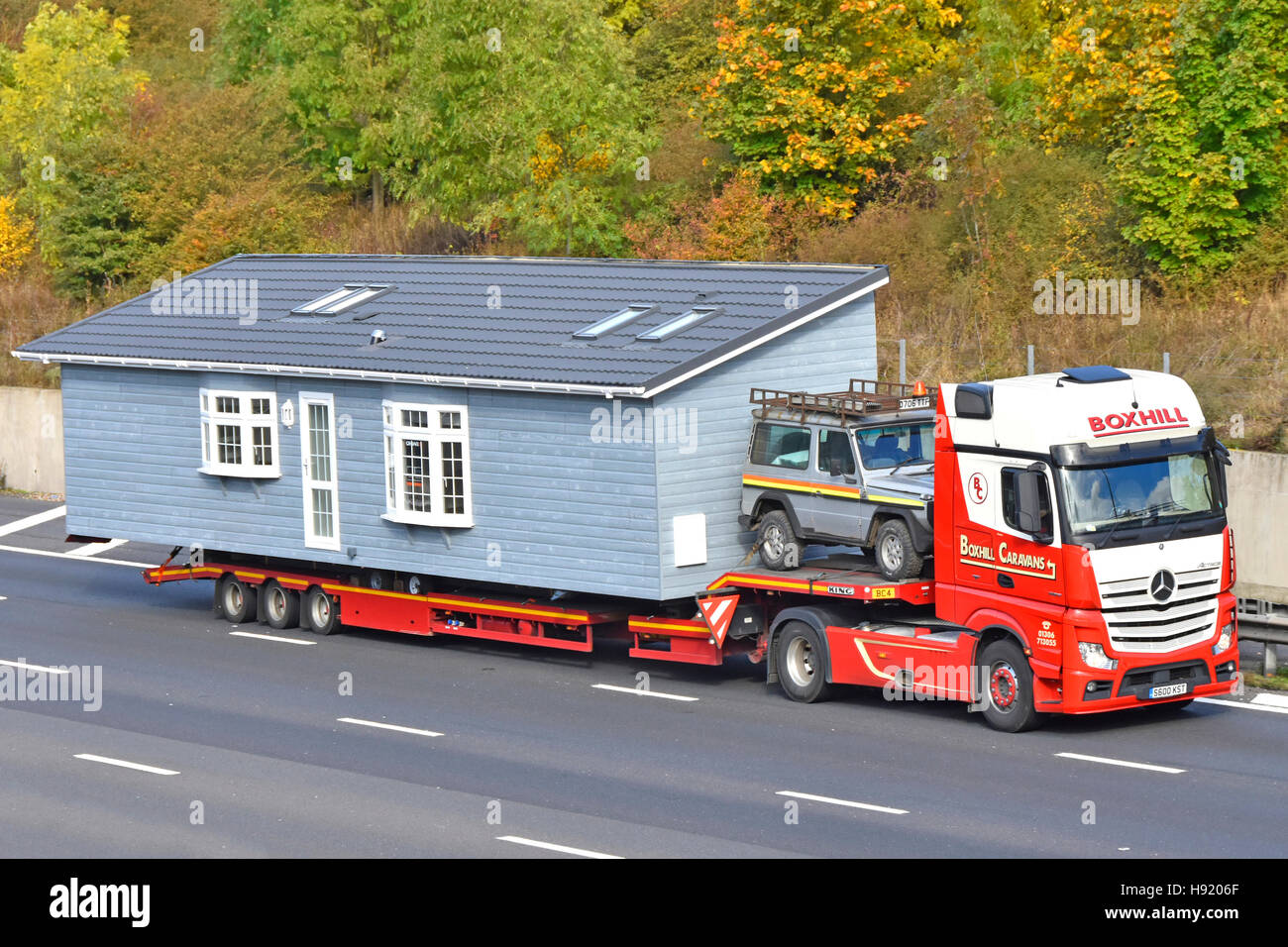 Part of oversize factory assembled prefabricated park home lodge wide load transported on UK motorway hgv low loader articulated truck with escort car Stock Photo