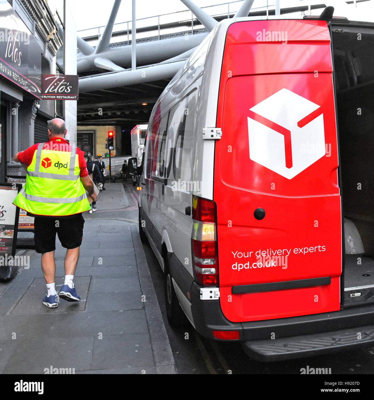 DPD logistics van delivery man driver carrying parcel to address in London England UK wearing health & safety high vis jacket Stock Photo