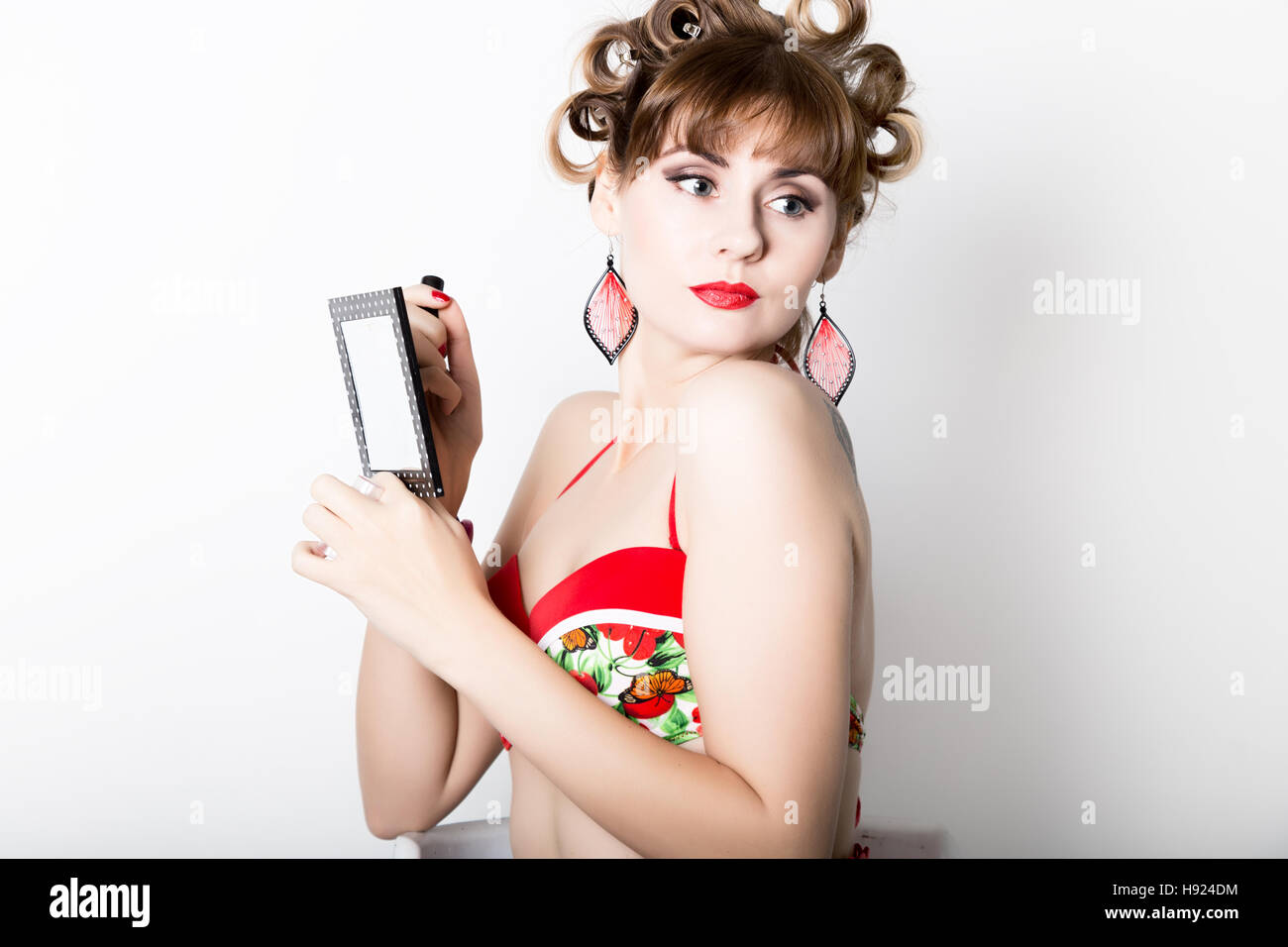 young beautiful woman preparing to party, girl styling hair with curlers looking in the mirror retro style Stock Photo
