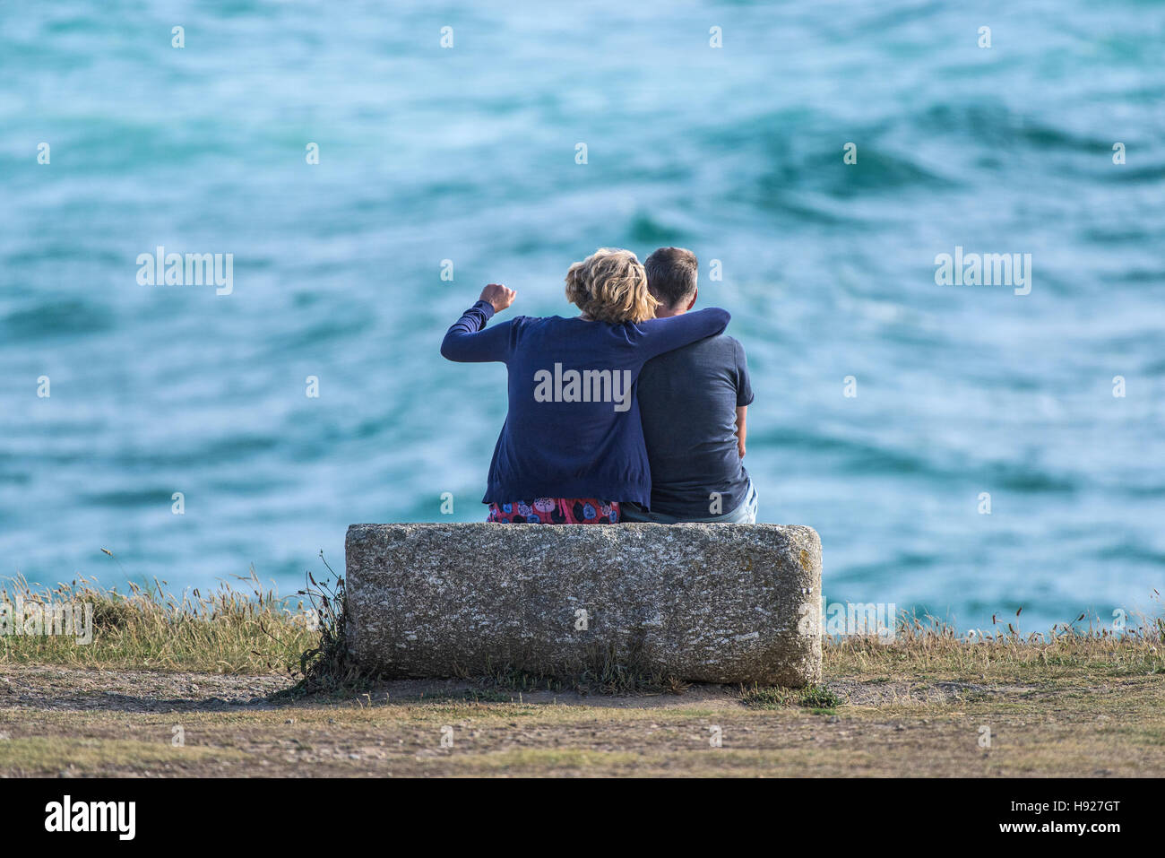 An affectionate couple sit and relax as they overlook the sea on the Headland in Newquay in Cornwall. Stock Photo