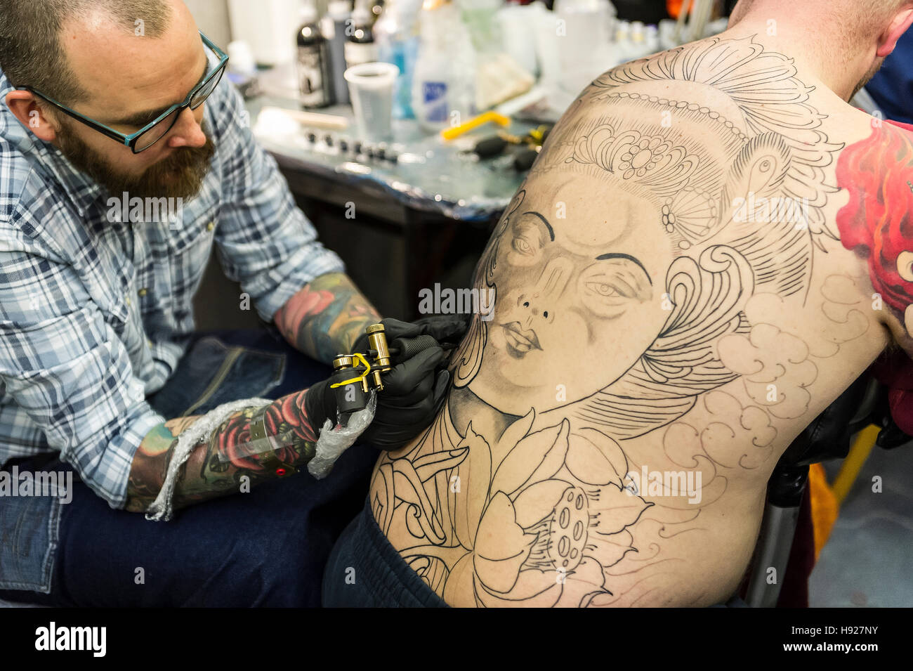 A tattooist inking a large design on the back of a customer. Stock Photo