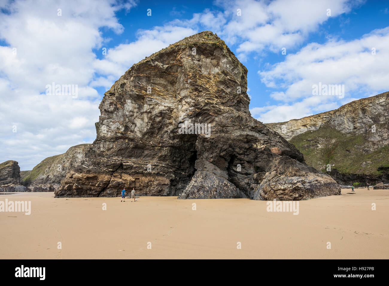 One of the iconic rock stacks at Bedruthan Steps towers over the tiny figures of tourists. Stock Photo